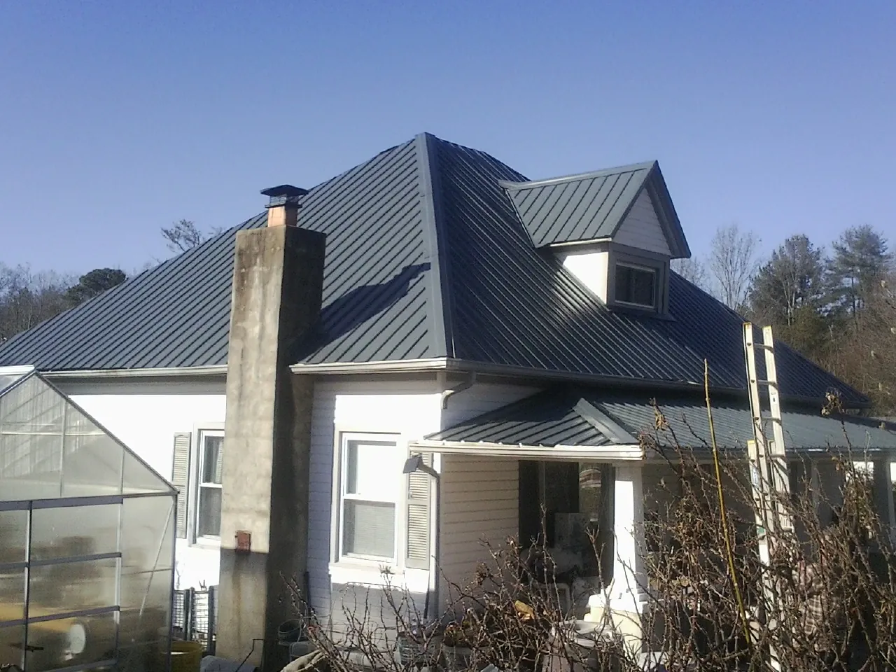 Dark blue standing seam metal roof on a white farmhouse with dormer — Slate & Tile Roof Repair by Roofing Brothers in Meacham