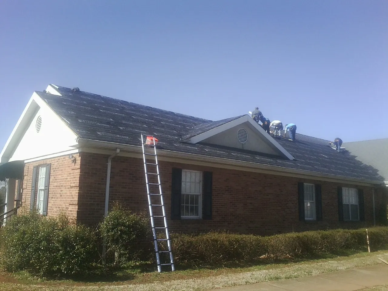 Crew tearing shingles off a brick ranch roof with a ladder set — Emergency Roof Repair work by our crew in Meacham