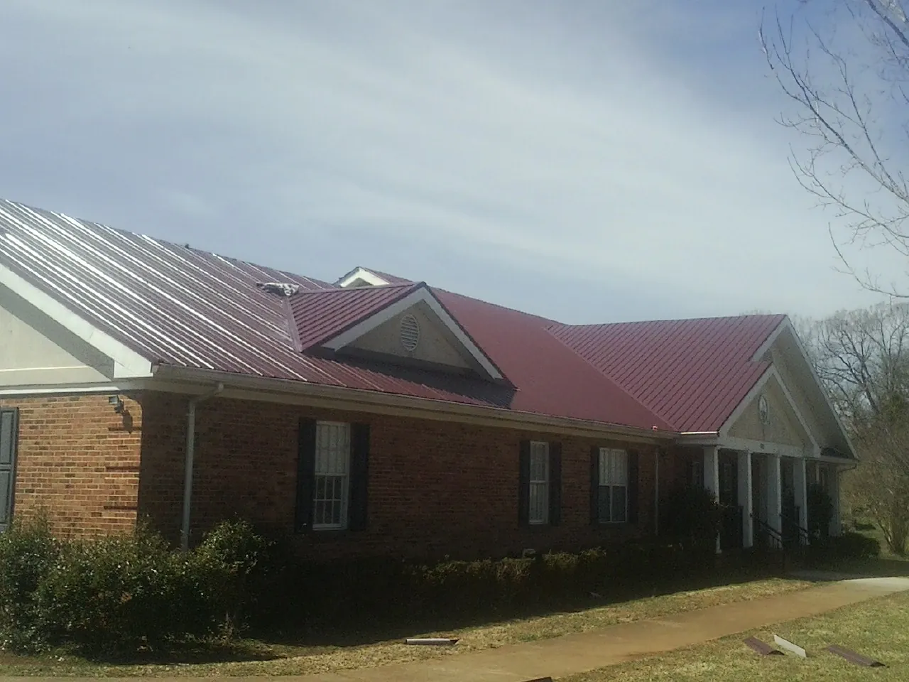 Red metal roof with gabled entries on a long brick building, from a Hail Damage Roof Repair job in Meacham