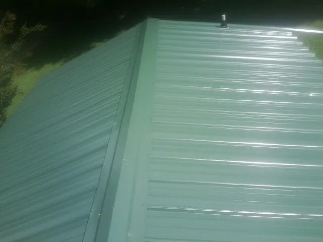 New green metal panels meeting at the ridge of a roof — Flat Roof Repair work by our crew in Meacham