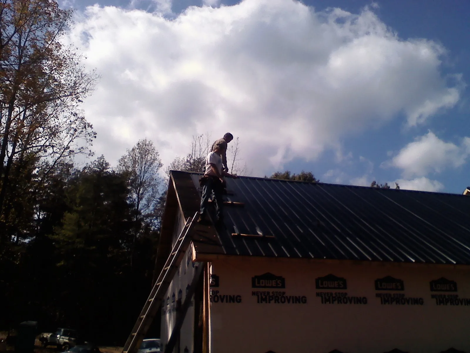 Roofer fastening dark metal panels high against a cloudy sky, from a Roof Inspection job in Meacham