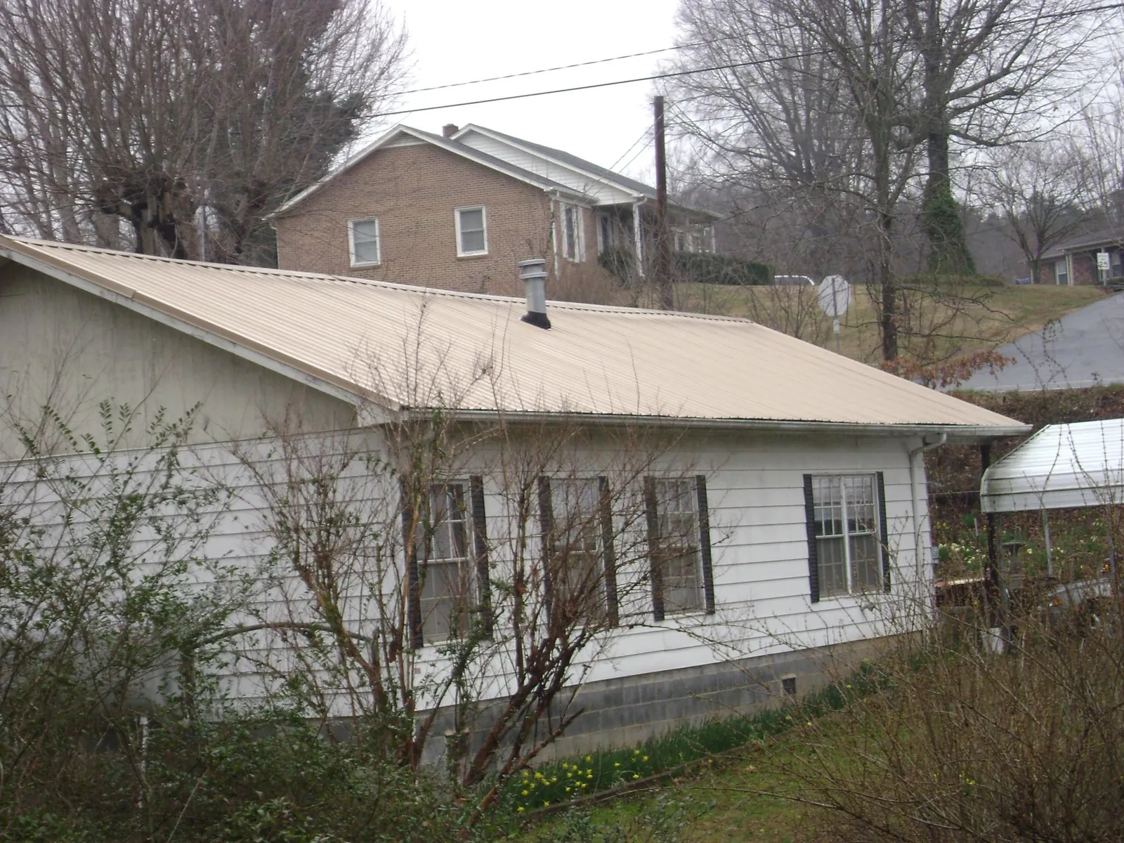 Tan metal roof on a white sided house set into a hillside — Commercial Roofing by Roofing Brothers in Meacham