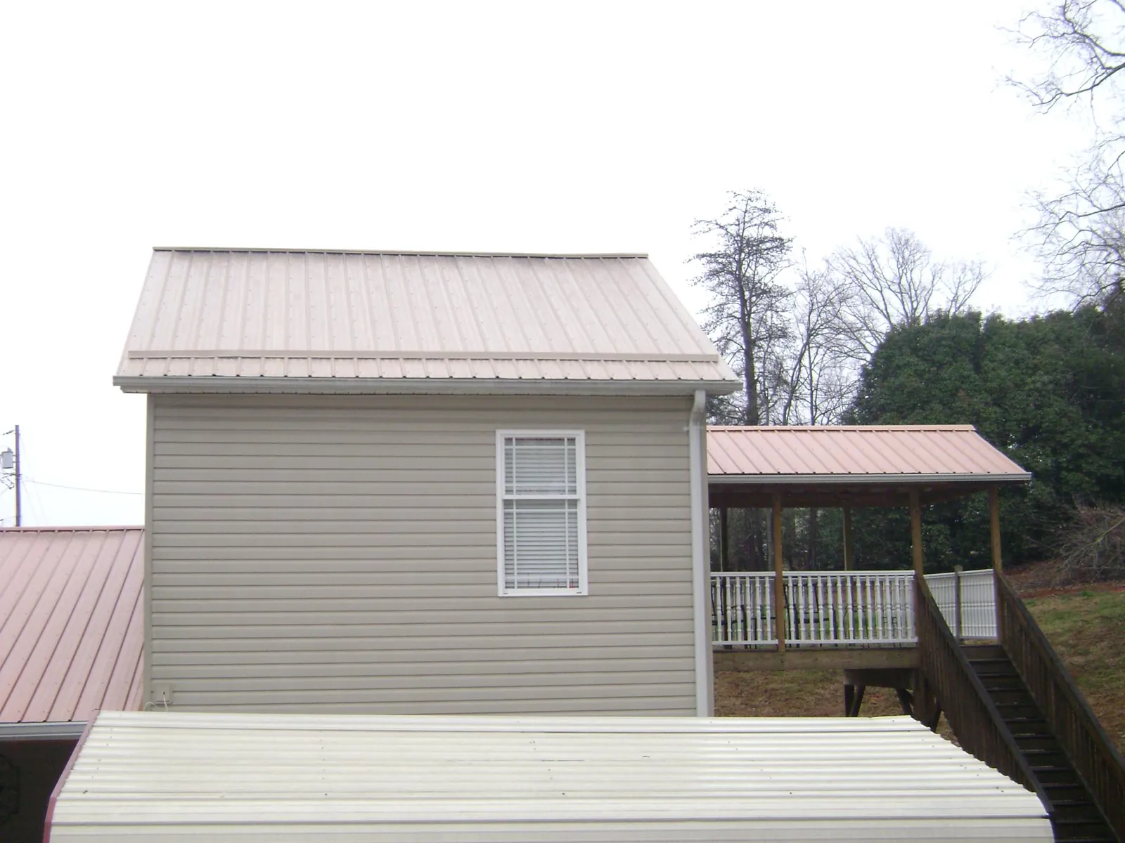Tan metal roofs on a two story addition and attached porch, from a Roof Replacement job in Meacham